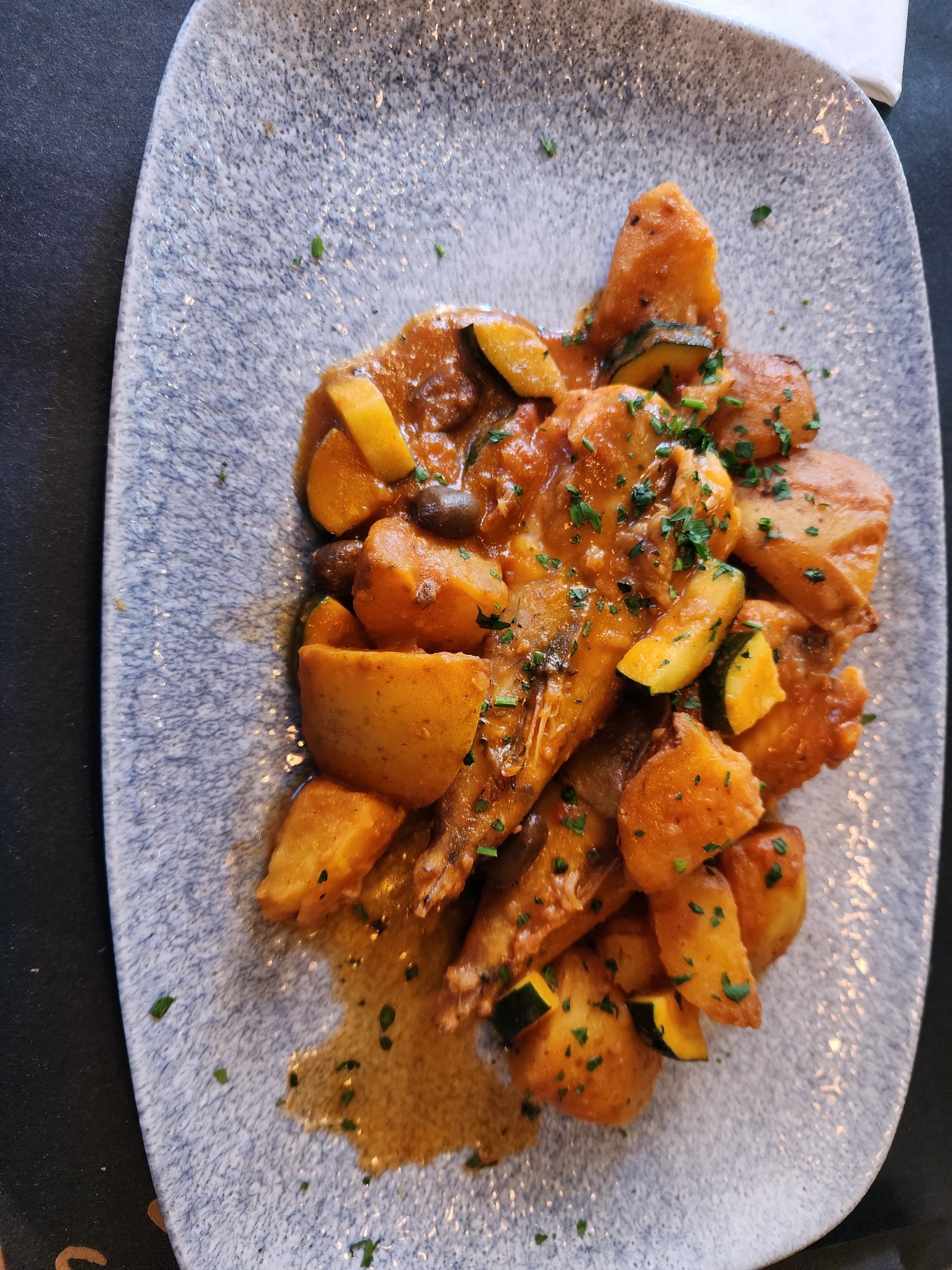 Slow-braised chicken in tomato sauce with roasted potatoes, zucchini, olives, and fresh herbs