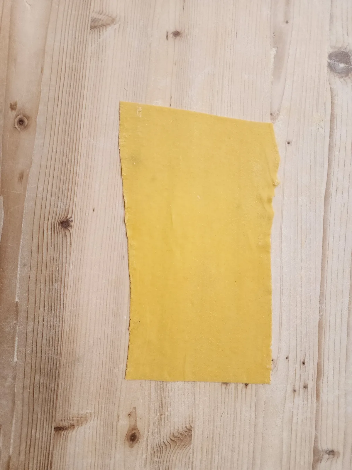 A fresh rectangular pasta sheet on a wooden work surface